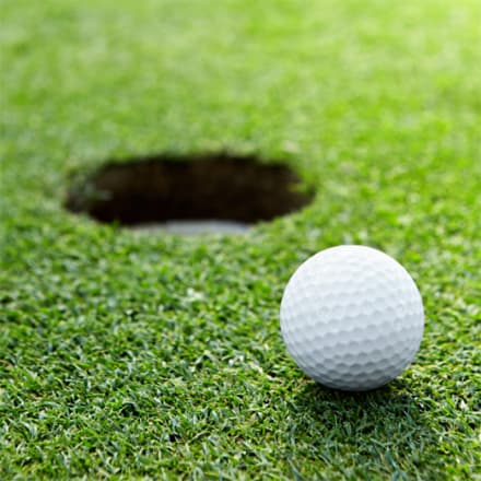 A golf ball inches away from a hole.