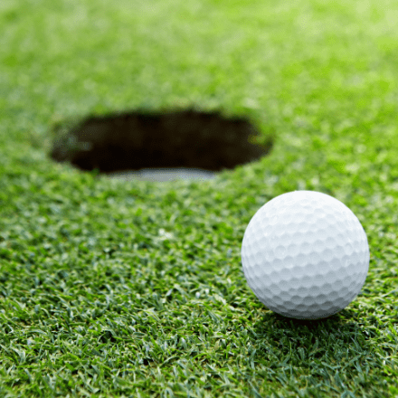 A golf ball on the green inches away from the hole.