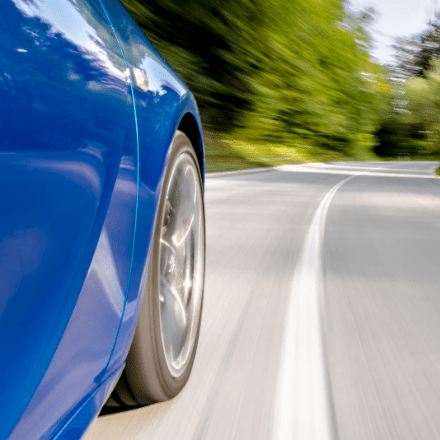 Side wheel view of a blue car driving on a winding road.
