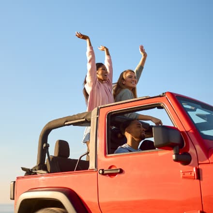 A smiling group of young adults in an orange Jeep.