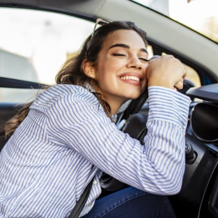 A woman hugging the steering wheel of a new car.