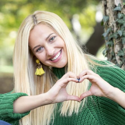 A blonde woman making a heart with her hands.