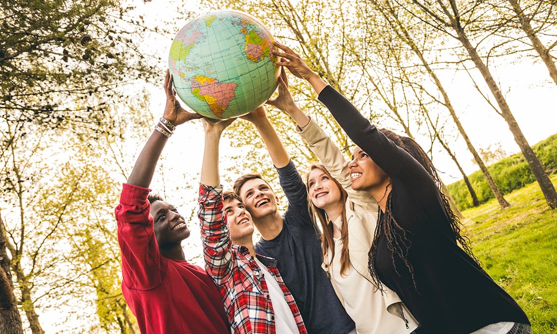 A group of young kids holding a globe with outstretched arms.