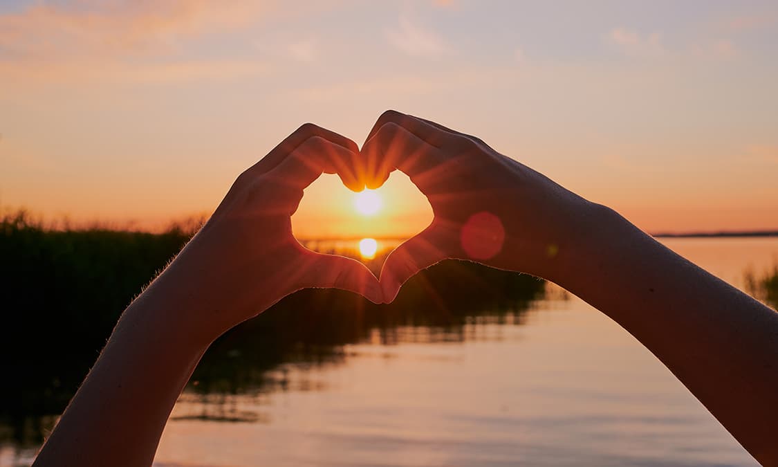 Two hands together in a form of a heart showing a sunset at the center.