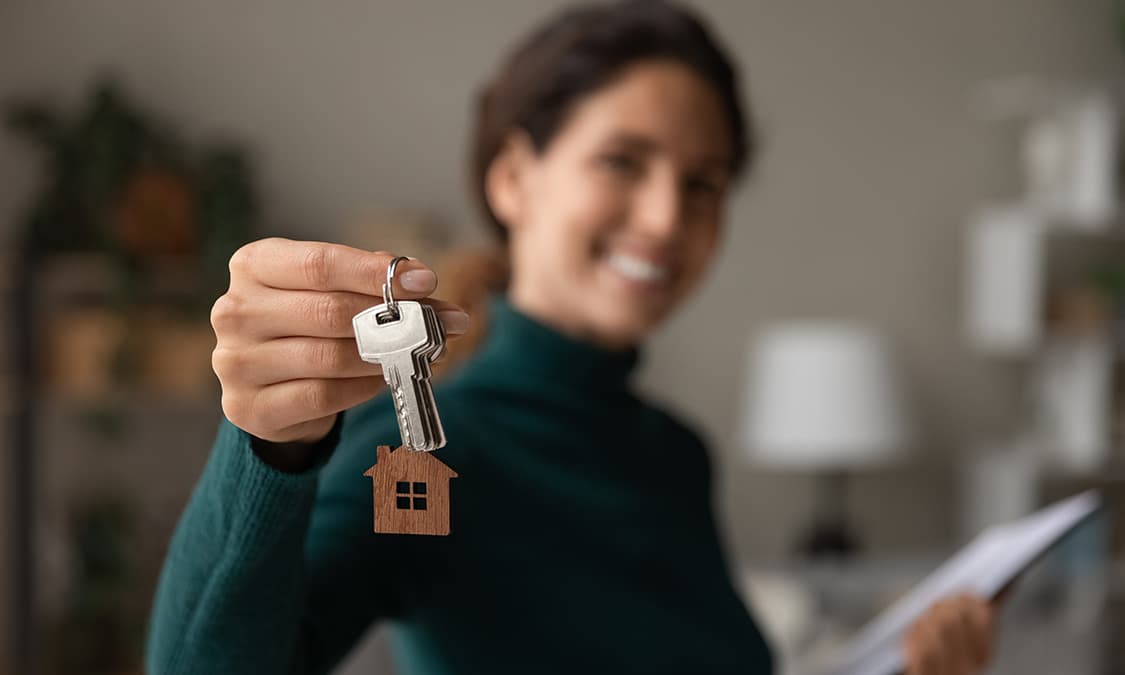A woman holding a keychain decorated with a wooden home.
