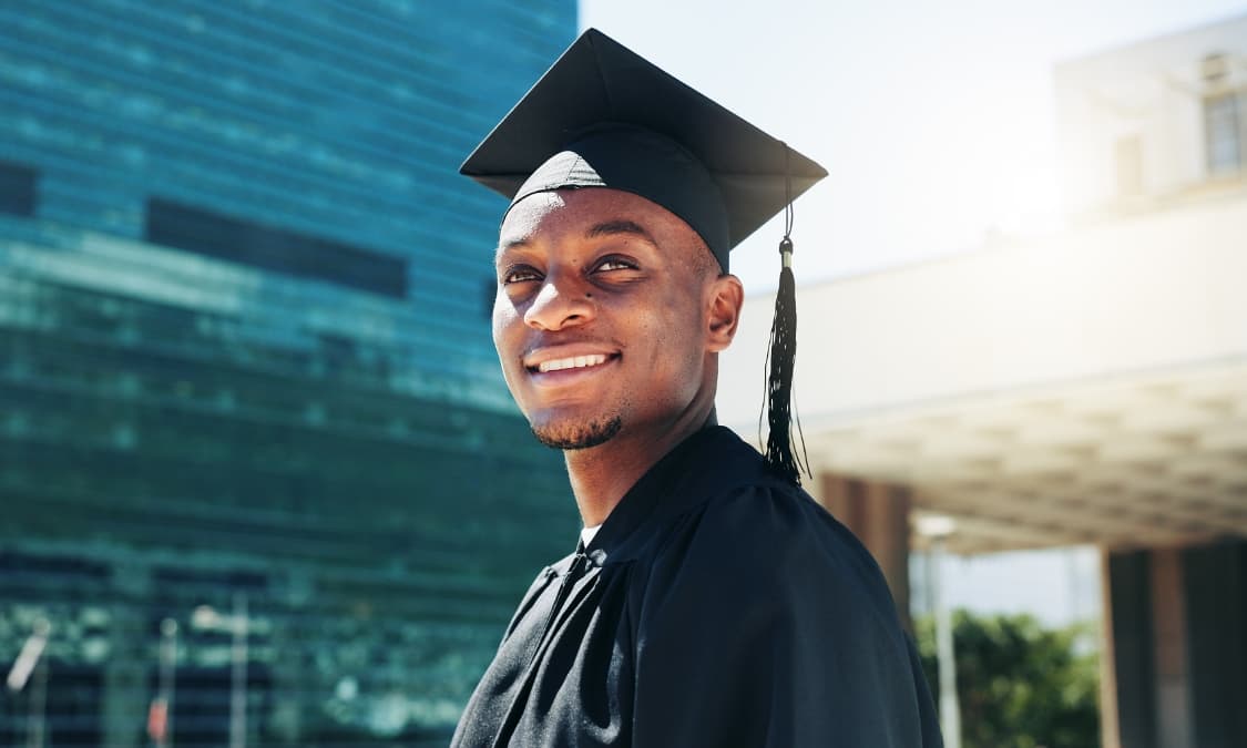 A smiling African American young man in a cap and gown.