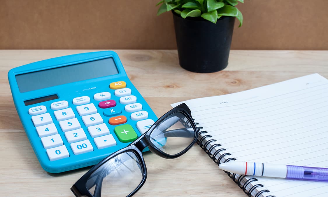 A calculator and a notepad resting on a desk.